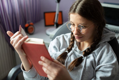 A smiling teenager with glasses reads a school reading at home.