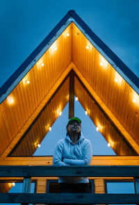 Man in front of illuminated wooden cabin looking at view