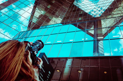 Low angle view of woman photographing against sky