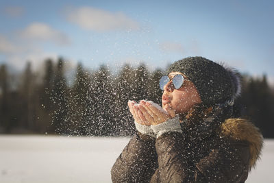 Young woman wearing sunglasses blowing snow