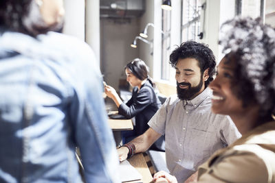 Happy business people having meeting with female colleague sitting in background