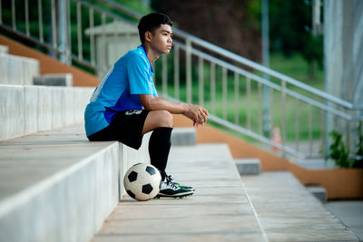 Side view full length of soccer player sitting on steps