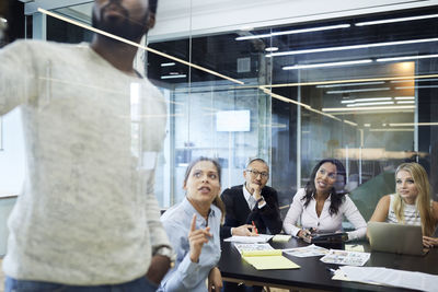 Multi-ethnic colleagues looking at entrepreneur giving presentation in meeting at board room