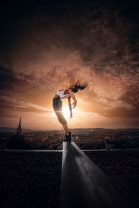 Side view of woman exercising against cityscape during sunset