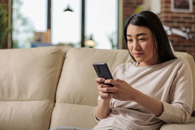 Young woman using mobile phone while sitting on sofa at home