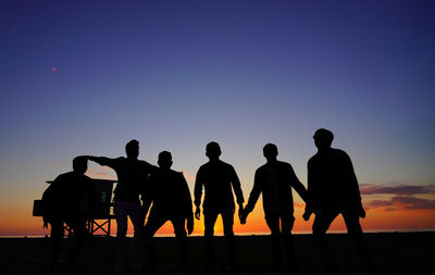 Silhouette people standing on land against clear sky during sunset