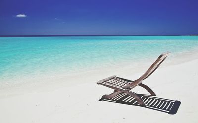 Wooden deck chair at beach against blue sky on sunny day