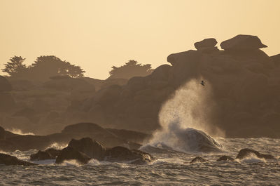 Waves splashing on rocks at shore against clear sky