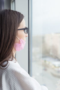 Close-up portrait of young woman looking through window