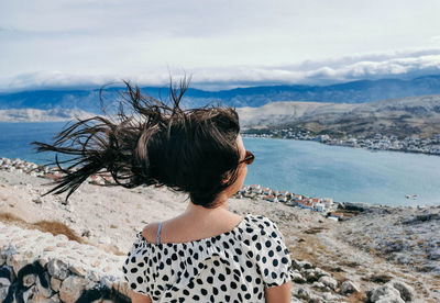 Rear view of young woman on viewpoint over sea. wind blowing hair.