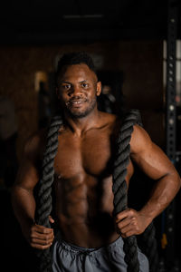 Muscular african american man posing with rope in gym. 
