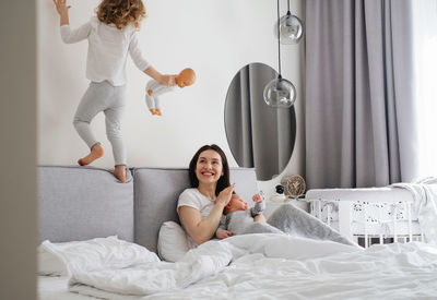 Mama with two kids at home in bedroom. baby infant resting on mothers hands, while older sister