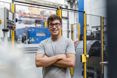 Smiling male engineer with arms crossed standing in illuminated industry