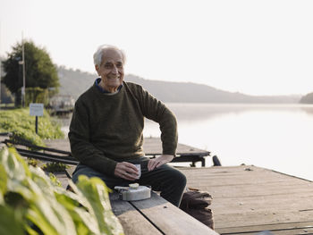 Portrait of smiling man sitting on shore against sky