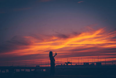 Silhouette person standing by sea against sky during sunset