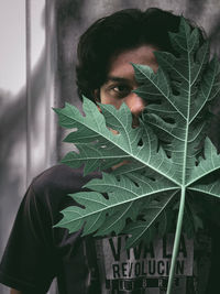 Portrait of young man holding leaf against face