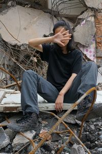 Full length of young woman covering face with hand while sitting on broken tile