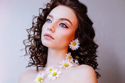 Close-up of beautiful young woman wearing flowers and make-up against wall