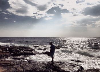 Man standing on rock at beach against sky