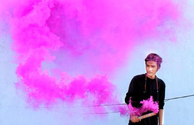 Man holding pink distress flare while standing against wall