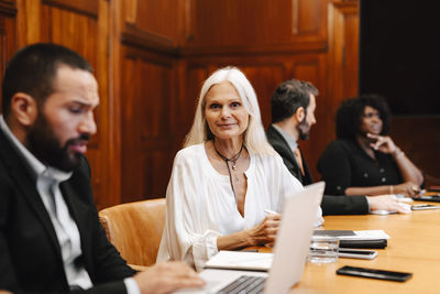 Portrait of smiling businesswoman sitting by businessman using laptop at conference table in board room