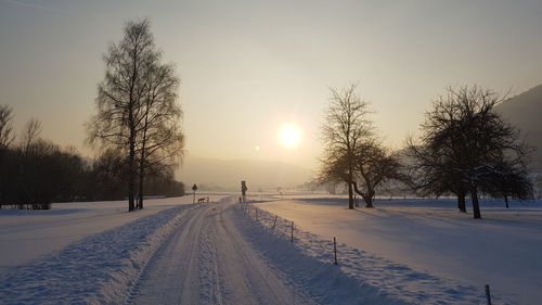 Road on snow covered landscape during sunset