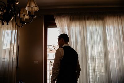 Rear view of businessman looking through window at home