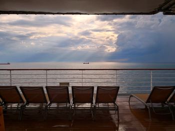 Empty chairs and table by sea against sky