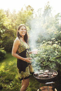 Happy woman standing by barbecue in back yard