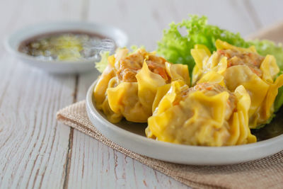 Chinese steamed dumpling, shumai on white dish served with soy sauce and lettuce leaves.