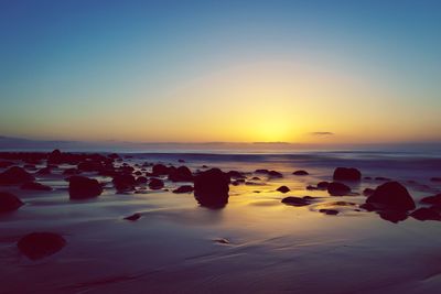 Rocks on beach against sky during sunset