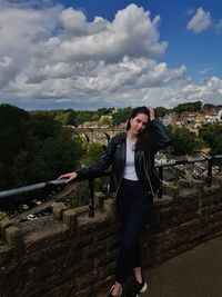 Portrait of young woman standing with arms outstretched against sky