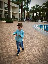 Full length of boy on footpath by palm trees