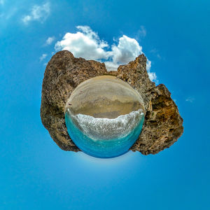 Little planet view of a rocky beach with clouds in the blue sky 