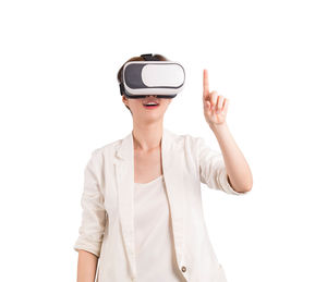 Young woman wearing virtual reality glasses while standing against white background