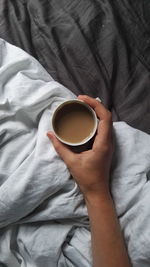 Midsection of woman holding coffee cup on bed