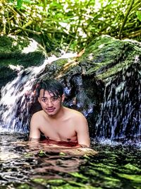 Portrait of shirtless young man looking at waterfall