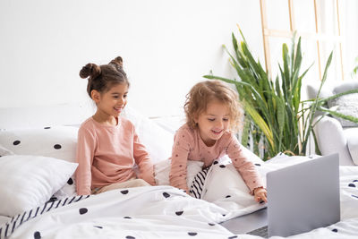 Cute little kids girls in pajamas using laptop in bed at home. kids using technology