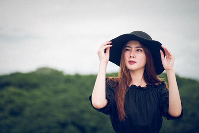 Young woman in hat standing against sky
