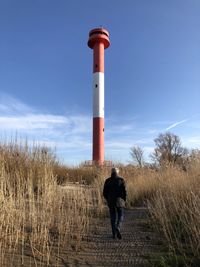 Man standing by lighthouse on field against sky