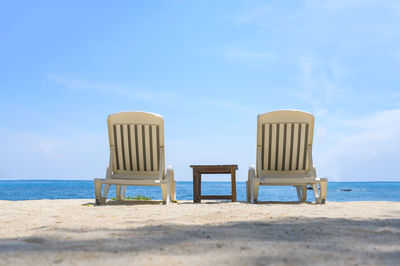 Empty chairs on beach against sky