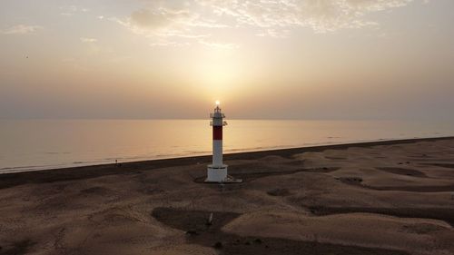 Lighthouse by sea against sky during sunset