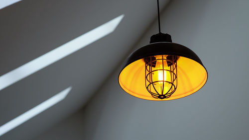 Low angle view of illuminated light bulb hanging on ceiling