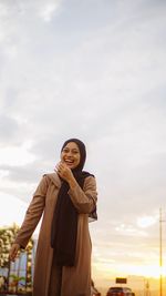 Smiling young woman standing against sky