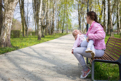 Mother and daughter fooling around while sitting on a bench in a city park.