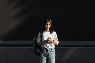 Portrait of smiling young woman standing against wall