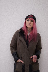 Young woman with pink hair standing against white wall