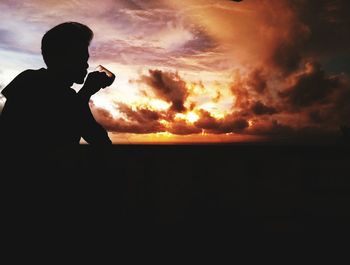 Silhouette man photographing against sky during sunset