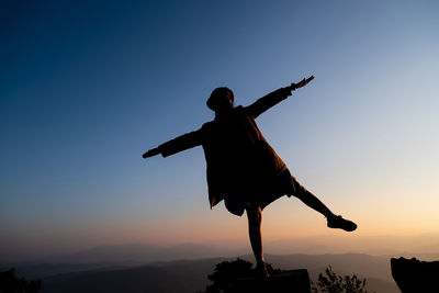 Silhouette man with arms outstretched against sky during sunset