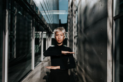 Portrait of young woman gesturing equal sign while standing against building